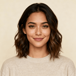 AI-generated portrait of a young woman with shoulder-length hair and natural makeup, wearing a simple casual top, posed with a gentle smile against a warm neutral background in diffused light.