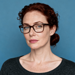 AI-generated portrait of a middle-aged woman with curly hair pulled back and glasses, wearing a dark knit top, posed with a calm expression against a cool slate background in soft moody light.