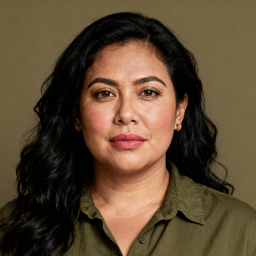 AI-generated portrait of a middle-aged woman with long dark hair, wearing a simple blouse, posed with a calm expression against a warm neutral background in soft light.