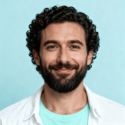 AI-generated portrait of a young man with short curly hair and light facial hair, wearing a light shirt, posed with an easy smile against a pale studio background in even lighting.