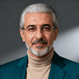 AI-generated portrait of an older man with gray hair, glasses, and a short beard, wearing a blazer over a turtleneck, posed with a calm expression against a soft gray background in studio lighting.