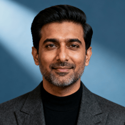 AI-generated portrait of a middle-aged man with neatly styled hair and light facial hair, wearing a blazer over a dark top, posed with a calm expression against a muted blue background in studio lighting.