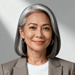 AI-generated portrait of an older woman with a sleek gray bob and defined features, wearing a blazer over a light top, posed with a gentle smile against a soft gray background in diffused studio lighting.