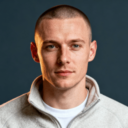AI-generated portrait of a young man with closely cropped hair and subtle freckles, wearing a quarter-zip pullover, posed with a neutral expression against a dark gray background in balanced lighting.