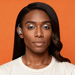 AI-generated portrait of a young woman with long styled hair and subtle makeup, wearing a light top and an ear-mounted hearing device, posed with a calm expression against a warm orange background in even studio lighting.