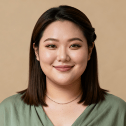 AI-generated portrait of a young woman with straight shoulder-length hair, wearing a simple blouse and necklace, posed with a gentle smile against a beige background in soft daylight.