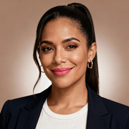 AI-generated portrait of a young woman with long hair pulled back and defined features, wearing a blazer and light top, posed with a warm smile against a neutral beige background in clean studio lighting.