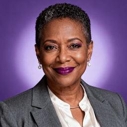 AI-generated portrait of a middle-aged woman with short cropped hair and defined features, wearing a blazer and blouse, posed with a warm smile against a purple background in clean studio lighting.