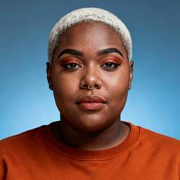 AI-generated portrait of a young woman with very short cropped hair and a nose ring, wearing a crewneck top, posed with a confident expression against a blue background in bright studio light.