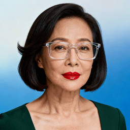 AI-generated portrait of a middle-aged woman with a short bob haircut and glasses, wearing a structured top, posed with a composed expression against a blue gradient background in bright studio light.