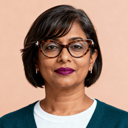 AI-generated portrait of a middle-aged woman with short straight hair and glasses, wearing a layered top and sweater, posed with a composed expression against a warm background in soft light.