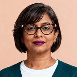 AI-generated portrait of a middle-aged woman with short straight hair and glasses, wearing a layered top and sweater, posed with a composed expression against a warm background in soft light.