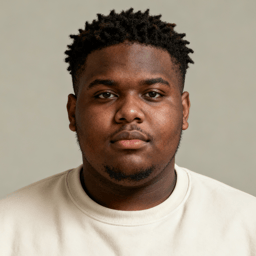 AI-generated portrait of a young man with short textured hair and a trimmed beard, wearing a light crewneck shirt, posed with a neutral expression against a warm neutral background in daylight.