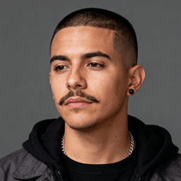 AI-generated portrait of a young man with closely shaved hair and a thin mustache, wearing a dark hoodie and chain necklace, posed with a neutral expression against a gray background in balanced light.
