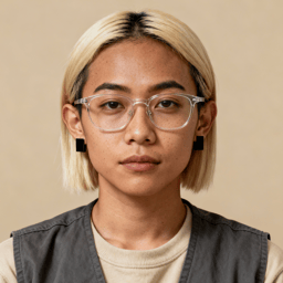 AI-generated portrait of a young woman with a blunt blonde bob and clear-frame glasses, wearing a layered top and vest, posed with a neutral expression against a warm beige background in natural light.