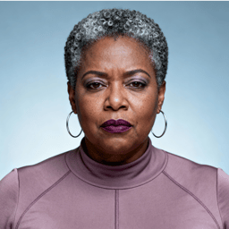 AI-generated portrait of a middle-aged woman with short curly gray hair and hoop earrings, wearing a high-neck technical top, posed with a neutral expression against a light blue background in cool diffused lighting.