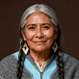 AI-generated portrait of an older woman with long gray hair in braids and subtle wrinkles, wearing layered wool garments, posed with a gentle expression against a dark neutral background in soft earthy light.