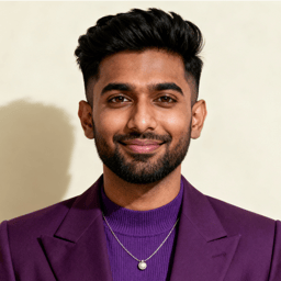 AI-generated portrait of a young man with styled dark hair and trimmed facial hair, wearing a blazer over a knit top and a necklace, posed with a relaxed smile against a light studio background in even light.