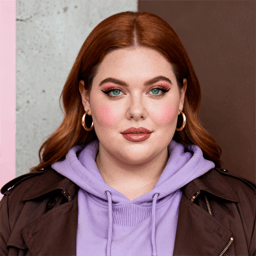 AI-generated portrait of a young woman with long softly waved hair, wearing hoop earrings, a hoodie, and a structured jacket, posed with a calm expression against a textured neutral background in soft studio light.