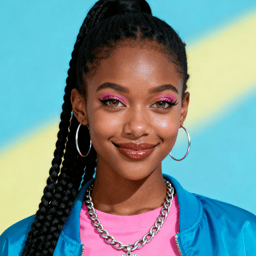 AI-generated portrait of a young woman with long braided hair and bold pink eye makeup, wearing a blue jacket and pink top, posed with a warm smile against a pastel background in bright studio light.