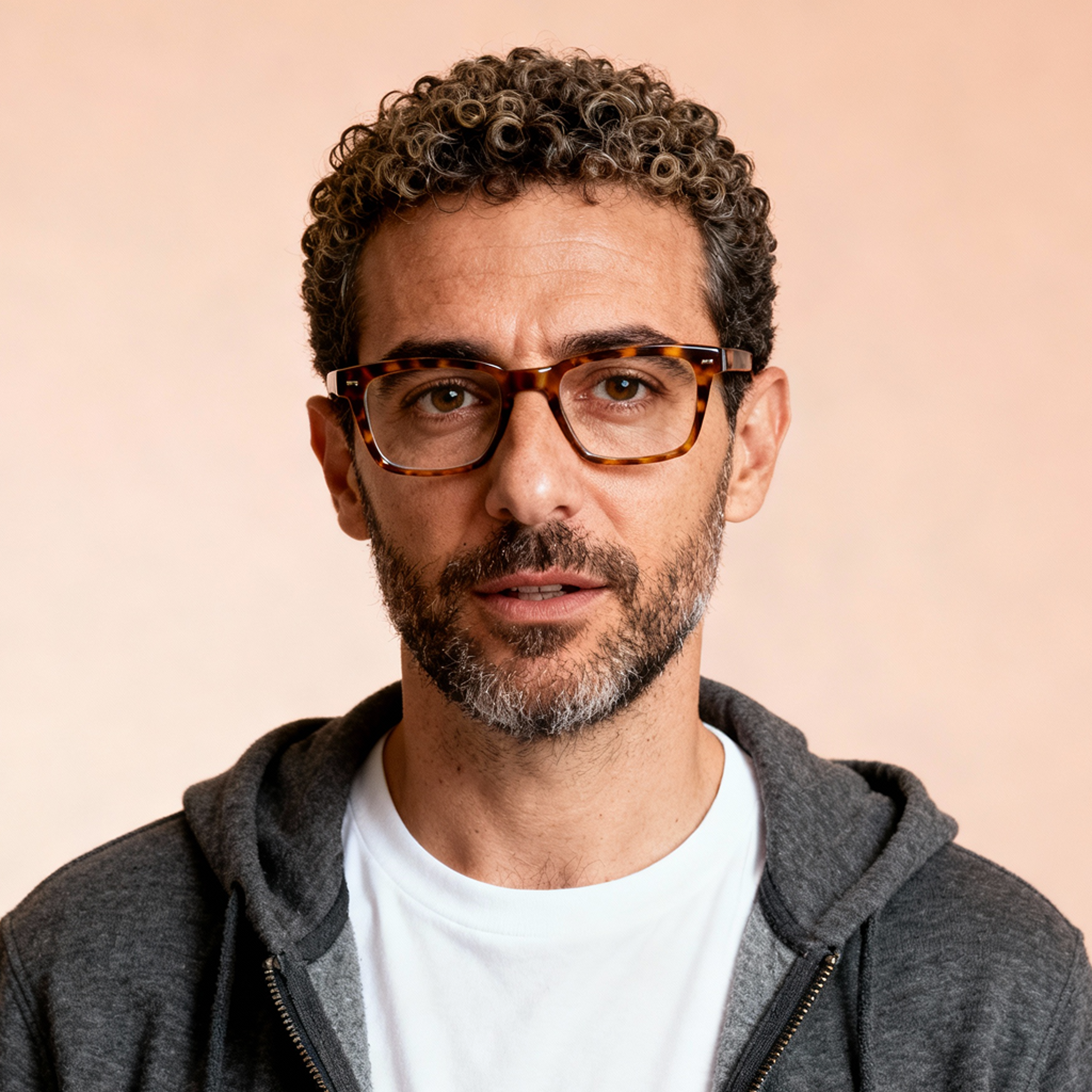 AI-generated portrait of a middle-aged man with curly hair, a beard, and glasses, wearing a hoodie over a t-shirt, posed with a relaxed expression against a neutral background in even light.