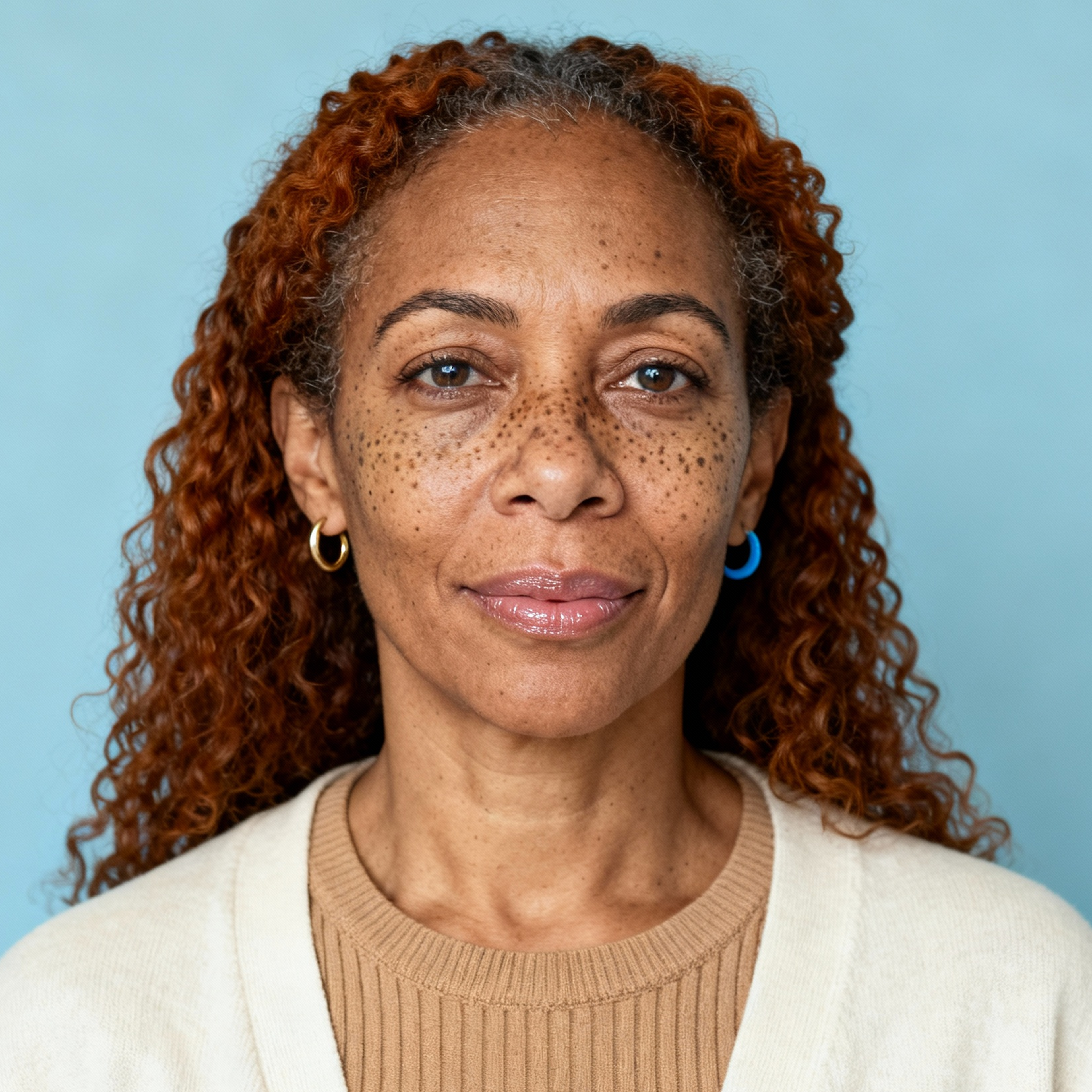 AI-generated portrait of a middle-aged woman with curly hair and freckles, wearing a simple top, posed with a neutral expression against a soft blue background in even light.