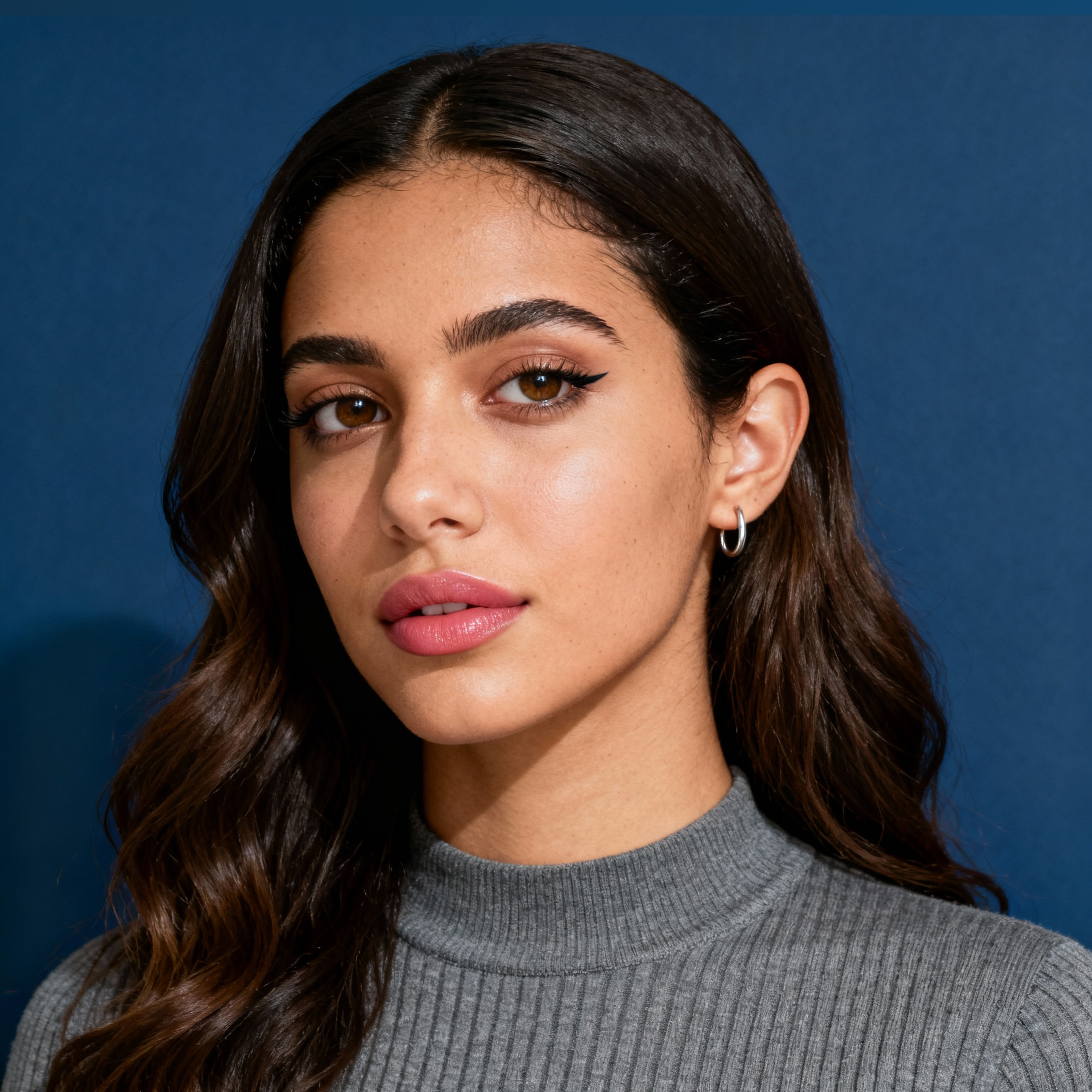 AI-generated portrait of a young woman with long dark hair and defined brows, wearing a simple knit top, posed with a neutral expression against a cool slate background in soft moody light.