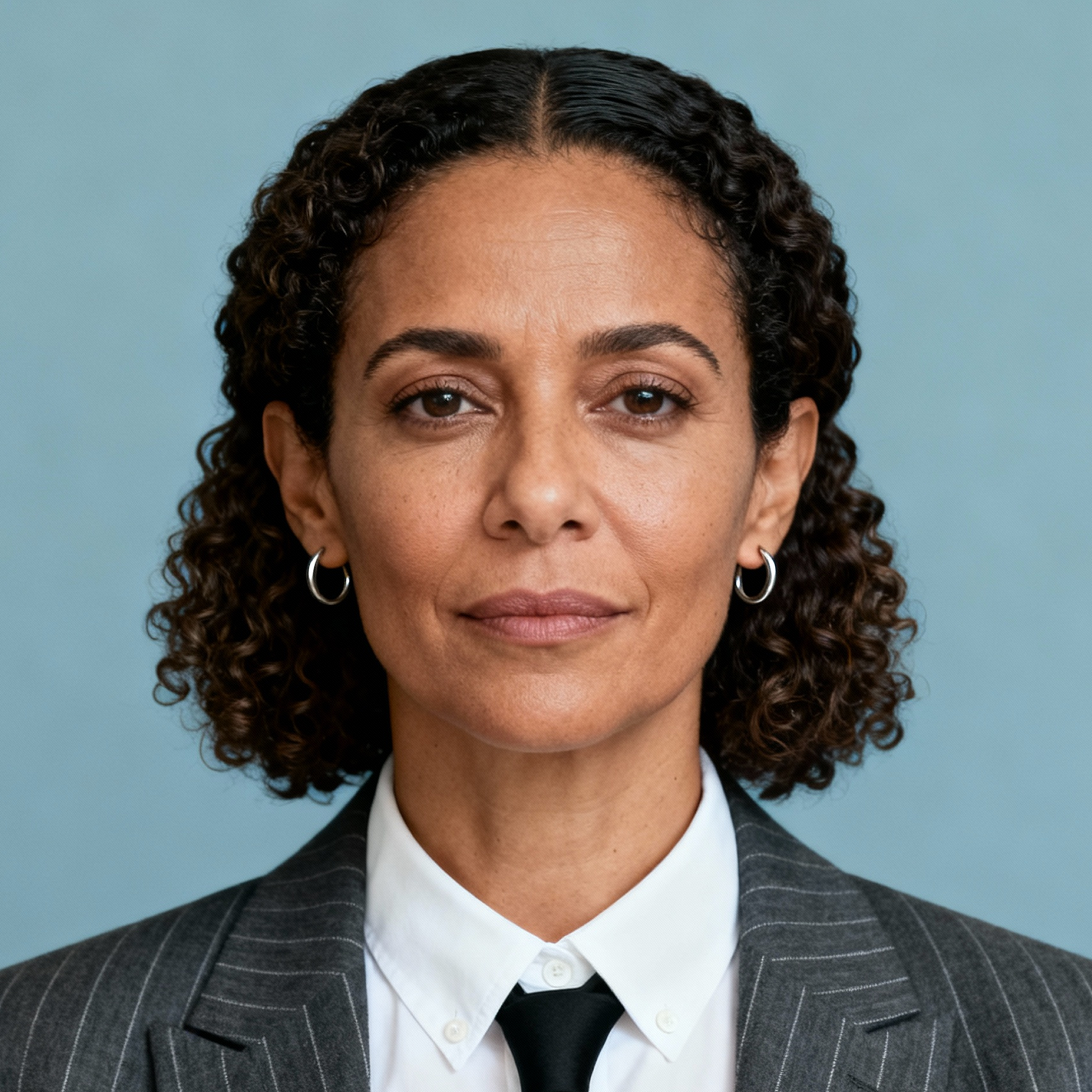 AI-generated portrait of a middle-aged woman with shoulder-length curly hair, wearing a blazer and collared shirt, posed with a neutral expression against a muted blue background in soft lighting.