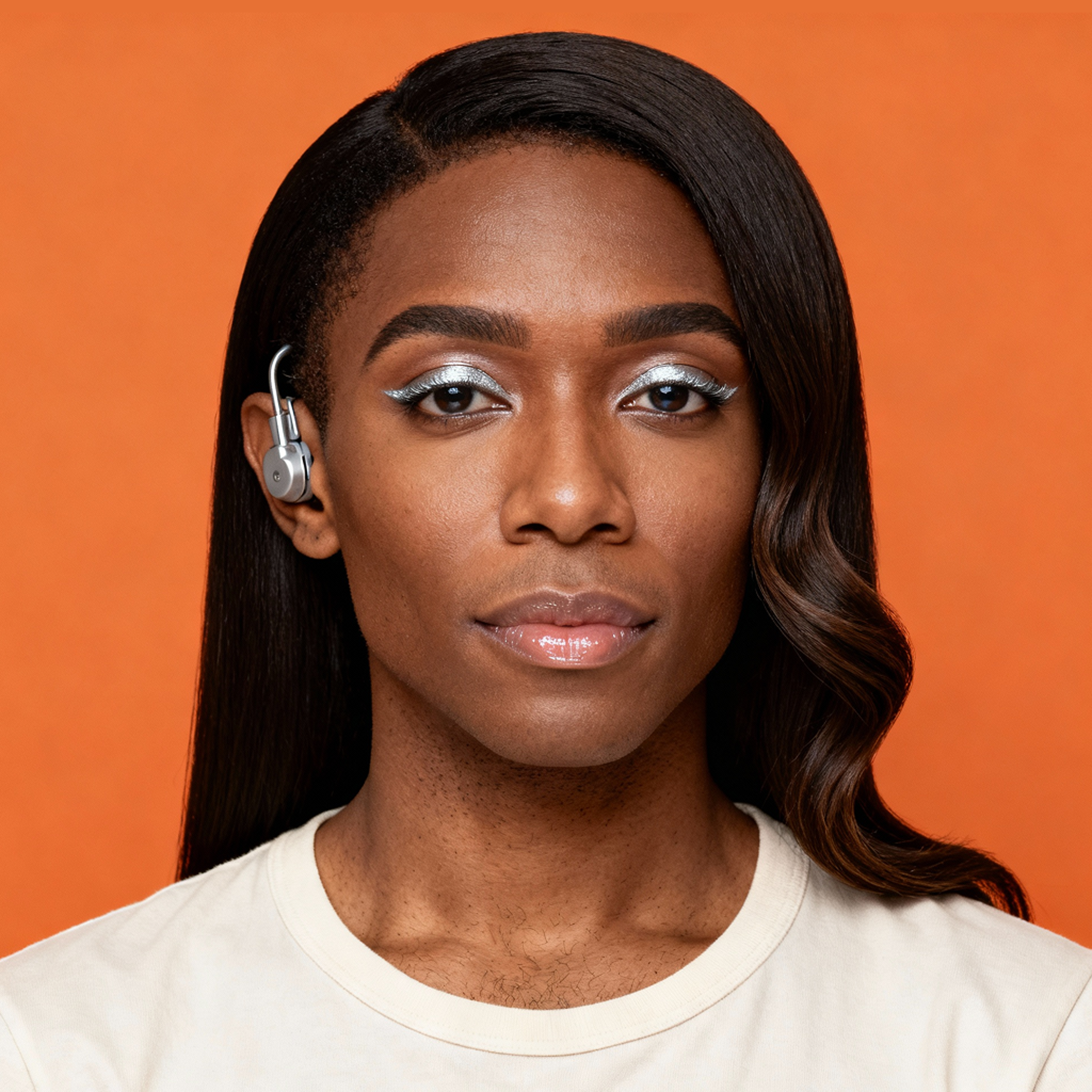 AI-generated portrait of a young woman with long styled hair and subtle makeup, wearing a light top and an ear-mounted hearing device, posed with a calm expression against a warm orange background in even studio lighting.