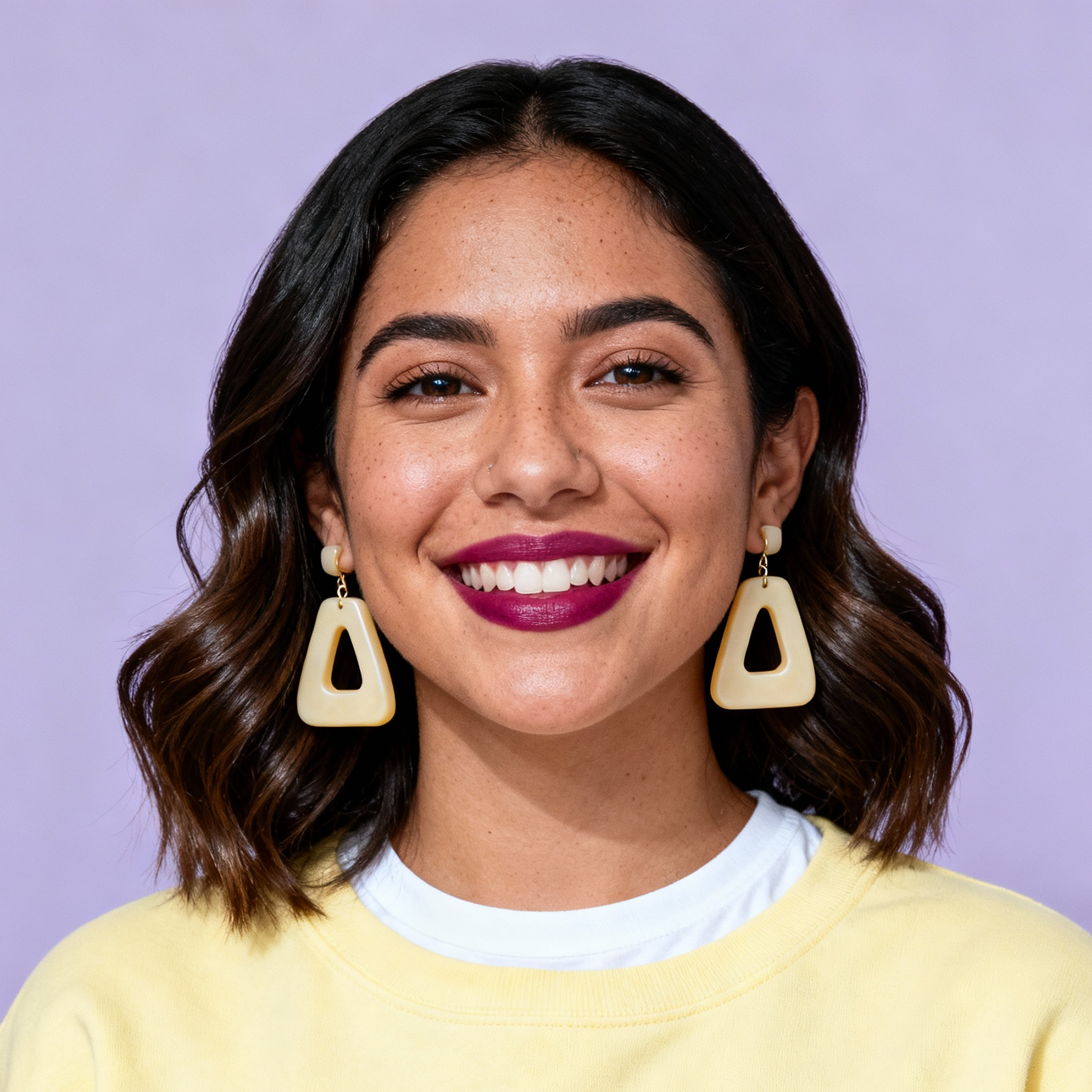 AI-generated portrait of a young woman with shoulder-length wavy hair and bold earrings, wearing a light sweater over a shirt, posed with a smiling expression against a soft lavender background in diffused studio light.
