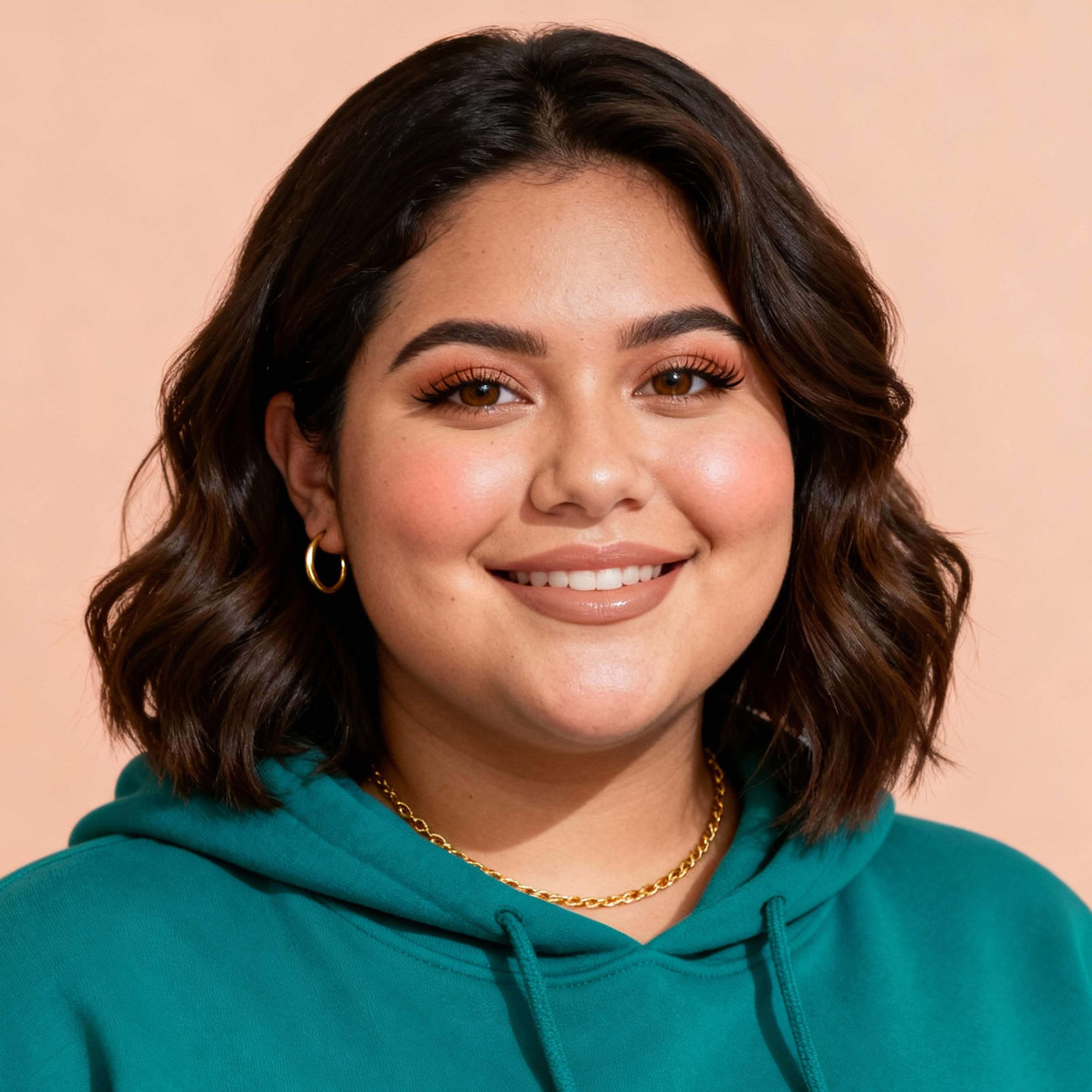 AI-generated portrait of a young woman with shoulder-length wavy hair and subtle makeup, wearing a green hoodie and gold necklace, posed with a calm expression against a soft peach background in natural light.