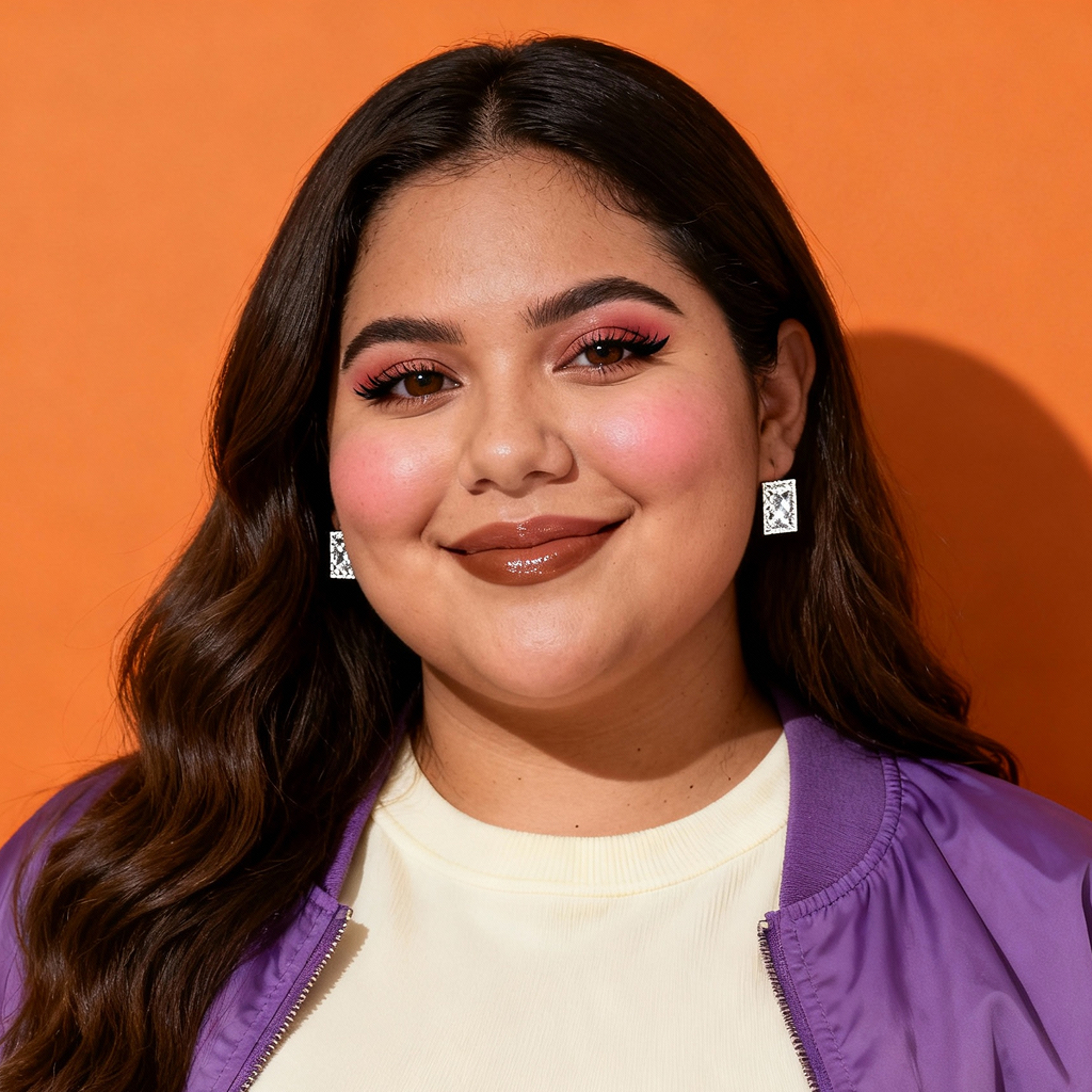 AI-generated portrait of a young woman with long softly waved hair, wearing square earrings and a casual jacket over a top, posed with a gentle smile against an orange studio background in even light.